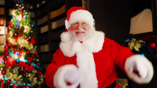Santa Claus uses headphones to listen to music and dances in a great mood.