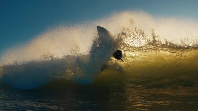 Wave breaks and boy surfer passes it holding his surf board. Surfing at sunrise