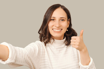 Nice smiling young woman is taking a selfie photo while showing thumb up.