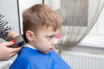 Nice european little boy getting hairstyle in barbershop.
