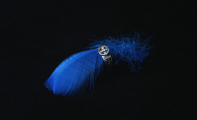 Silver engagement ring with diamond on blue feather. White gold ring with gemstone on black background. Wedding fashion jewellery