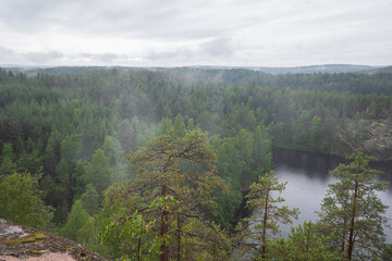 Soft focus image of fog raising over the lake, rocks and forest in the Repovesi National Park after the rain on cloudy summer day. View from Katajavuori Hill