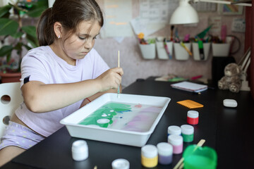 an attractive girl of primary school age of European appearance paints on the water in the ebru technique. The concept of children's creativity