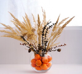  Natural spruce bouquet with dry decor and pampas in vase with tangerines on white windowsill by...
