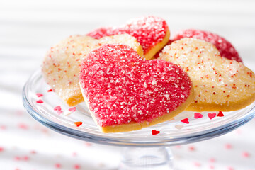 Heart shaped sugar cookies with white, pink, and red sugar sprinkles on a glass tray