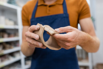 cropped view of man in apron modeling clay piece during pottery class.