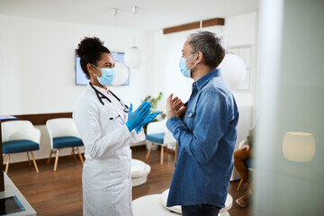 Obraz premium Happy patient and black female doctor wear face masks while communicating in waiting room at medical clinic.