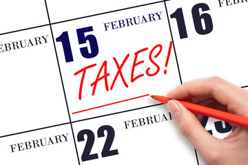 Hand drawing red line and writing the text Taxes on calendar date February 15. Remind date of tax payment