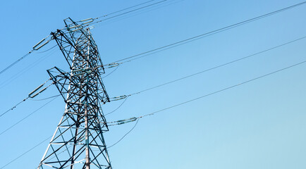 Steel power pylon construction with high voltage cables against blue sky.