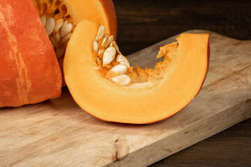 A slice of orange pumpkin with seeds lies on a wooden board
