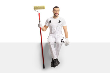 Painter holding a paint roller and sitting on a blank panel