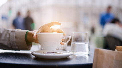 Fototapeta premium A hand reaches for vending coffee cup on table at street cafe 
