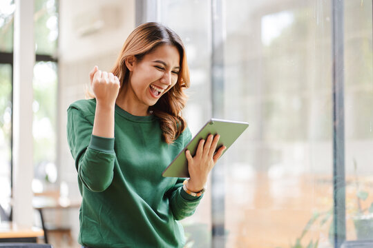 Asian girls are excited about victory. hand holding a digital tablet at her office