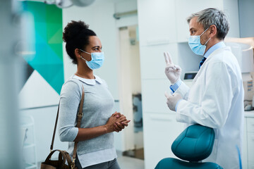 Black woman communicating with her dentist after dental procedure during coronavirus pandemic.