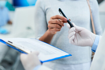 Close up of woman signing medical agreement before procedure at dentist's office.