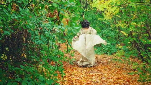 Princess girl runs in autumn park, steps on fallen yellow orange leaves of tree forest path, Vintage golden dress fabric train fly in motion. Escape of fantasy woman queen. Back view. Autumn nature