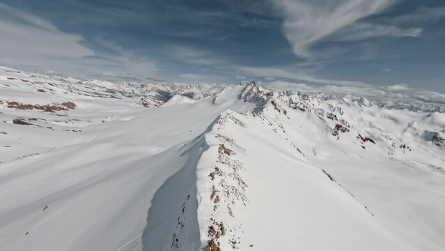 FPV sport drone flying over picturesque mountain ridge snowy rock texture sun light blue sky landscape. Aerial view empty alpine scenery winter glacier freeze valley natural cliff range freeze summit