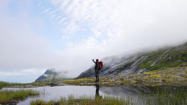 Man travel blogger taking photo by smartphone hiking with backpack in mountains influencer lifestyle adventure summer tour outdoor in Norway lofoten