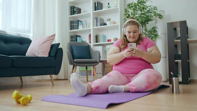 Gadget addicted overweight woman scrolling smartphone instead fitness training