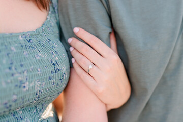 A couple with female hand's around man's arm, showing off her engagement ring.