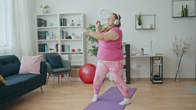 Excited plus size young woman dancing, listening music in headphones, having fun