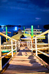 pier at night, some boats on the water and brigh lights in the background, coyuca lagoon in pie de la cuesta, acapulco guerrero 