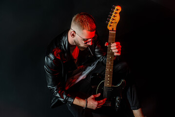 Rocker in leather jacket enjoying his guitar on black background.