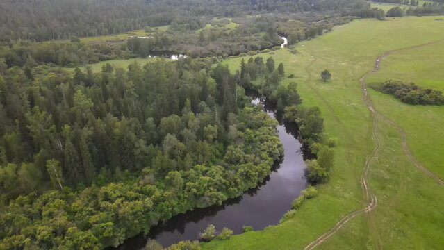 Aerial drone shot of Bratsk Siberia summer river in the green field, with trees around