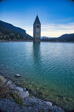 Vertical shot of the church tower at the shore of Lake Resia