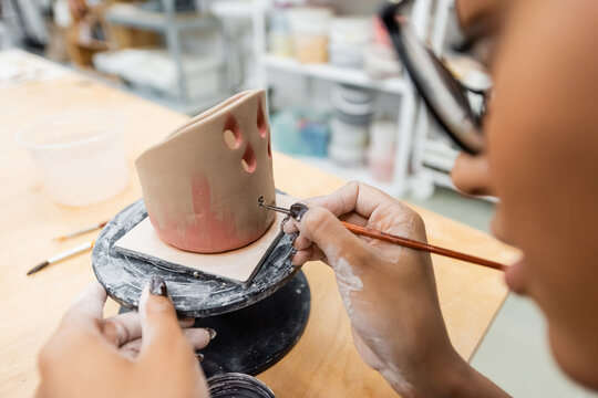 Blurred african american woman painting on ceramic sculpture in workshop.