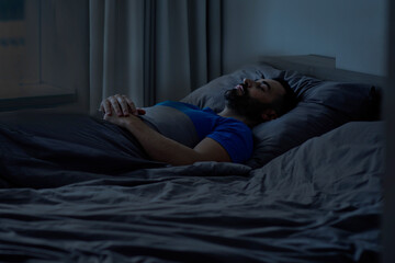  Side view of a young European man sleeping well and resting in bed at night