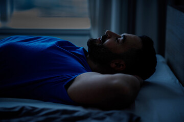 Arab young man sleeping lying on his back holding his hands on his head resting in bed in the...