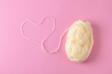 Top view of heart made from a woolen thread with ball of yarn on light pink background