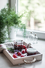 Jars with strawberry jam, strawberries and flowers on a linen towel and glass bottles.