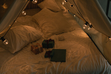 Gifts on camping tent bed decorated with Christmas lights. Kid's bedroom. Winter holidays. Evening...