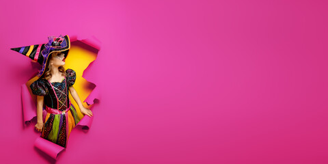 a little girl in a witch costume peeks out of a hole in a paper background