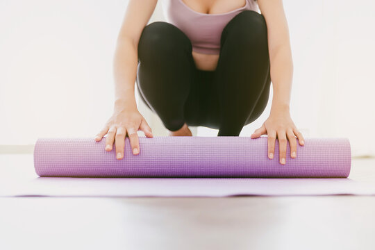 Crop image of woman hands rolling yoga mat, preparing for doing yoga. Working out at home or in yoga studio. Healthy habits, keep fit, weight loss concepts. Focus on hands on a mat.