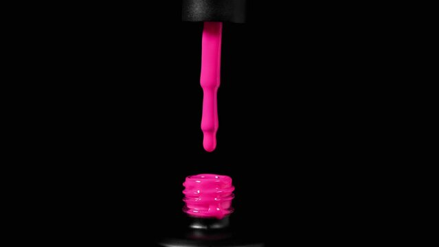A drop of pink gel nail polish dripping from a brush into a bottle