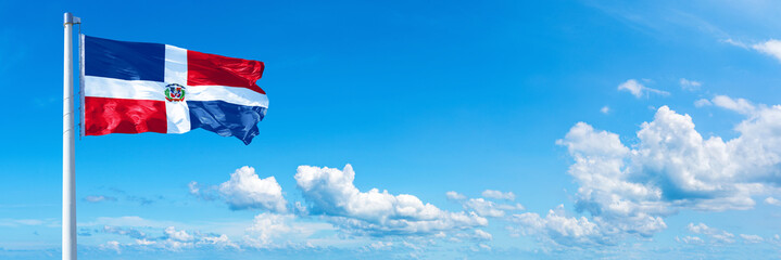 Dominican Republic flag waving on a blue sky in beautiful clouds - Horizontal banner
