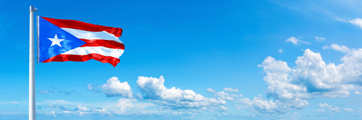Puerto Rico flag waving on a blue sky in beautiful clouds - Horizontal banner