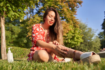 woman putting sunscreen on body sitting on grass