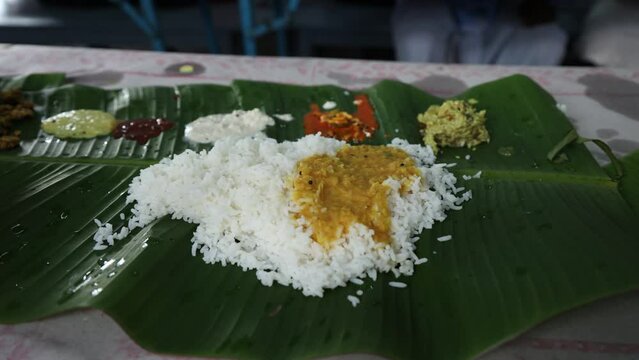 People eating traditional Indian wedding marriage sadhya rice Sambar, parippu dal curry ghee Payasam on banana leaf Onam Vishu Pongal Diwali festival vegetarian food Kerala Tamil Nadu South India.