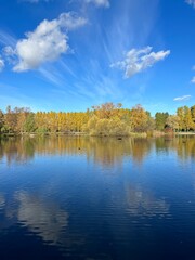 Autumn trees silhouettes reflection on the surface of the lake, blue sky