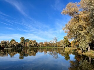 Autumn trees silhouettes reflection on the surface of the lake, blue sky