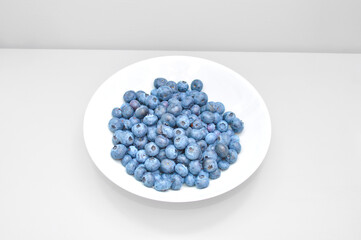 bunch of blueberry berries in a white plate on a light gray background
