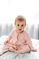  Girl baby  in pink pajamas on bed.