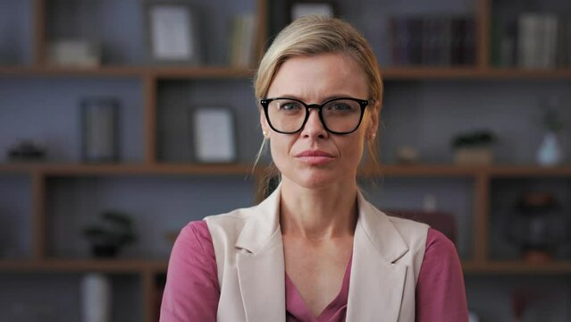 Portrait of beautiful blondie woman looking at camera and smiling. Adult stylish businesswoman wearing eyeglasses in office. Successful confident female leader close up face headshot, front portrait.