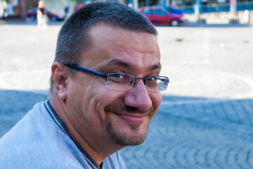 Portrait of a white man outdoors. The man is 58 years old, smiling and wearing prescription glasses.