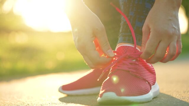 Woman tying shoelaces while jogging or walking at sunset. Slow motion