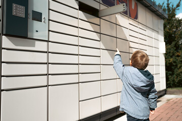 Pickup parcel. Child showing open door box at post delivery automat terminal. Self service post...